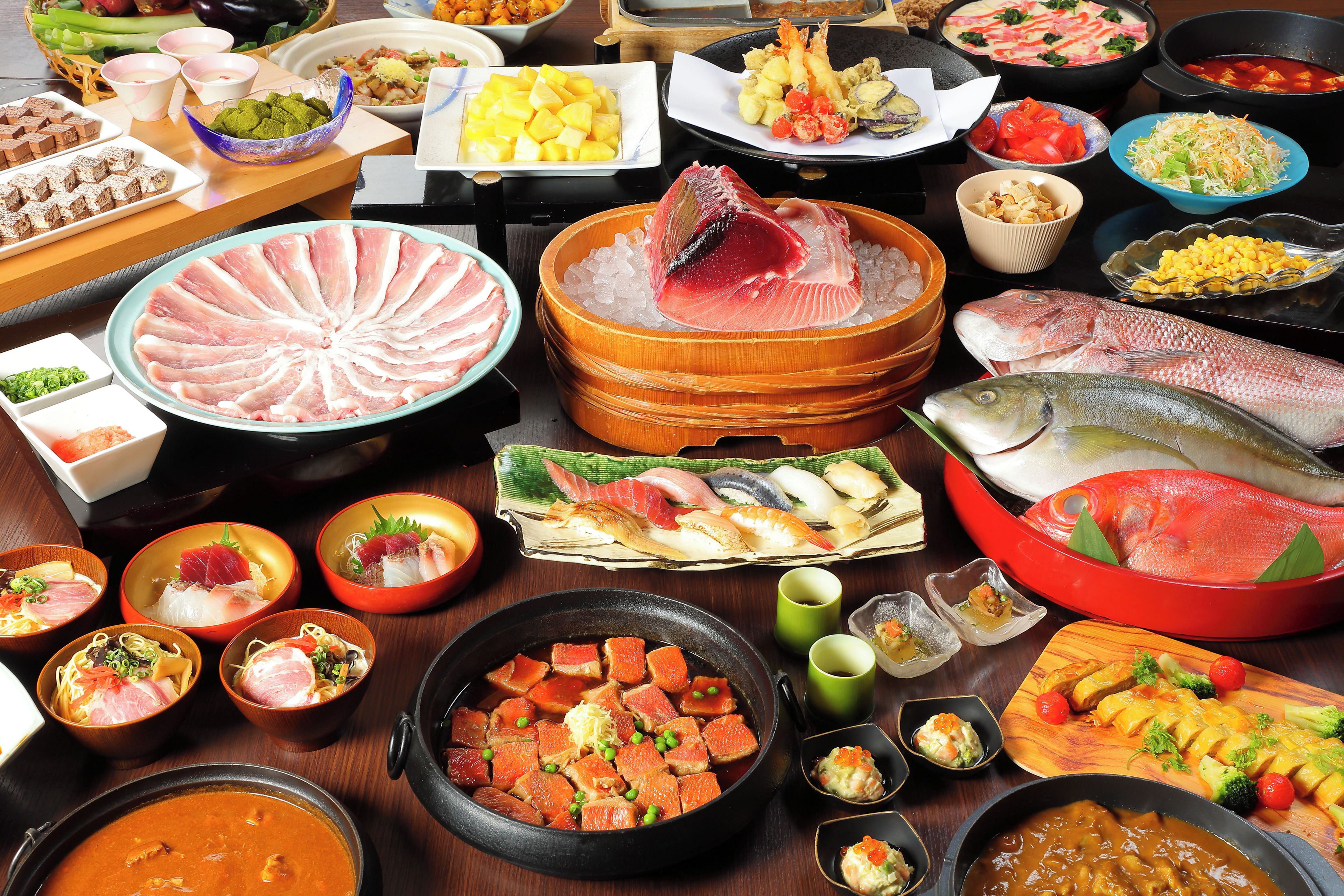 A variety of dishes and food items, including sushi, sashimi, and other seafood preparations, arranged on a table.