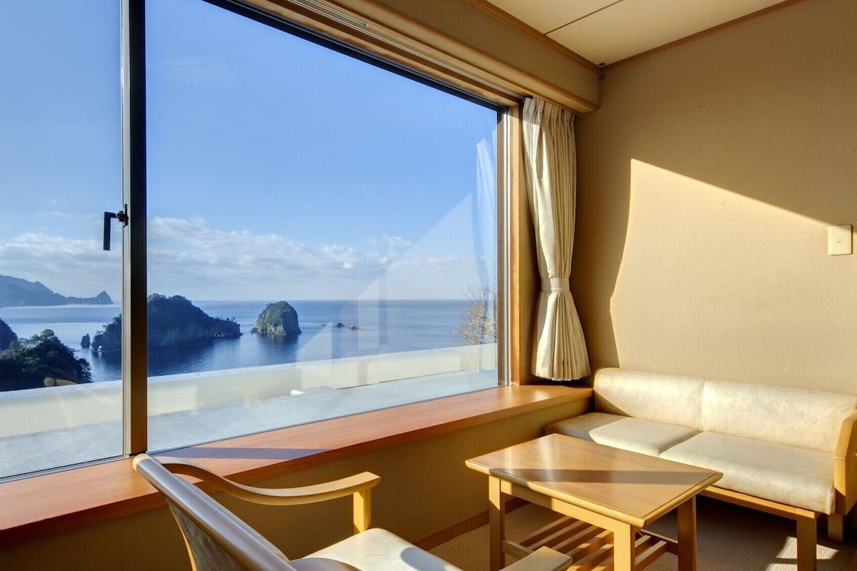 A hotel room with a large window offering a view of the sea and islands. There is a sofa and a small table.