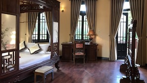 Ein traditionell eingerichtetes Schlafzimmer mit einem Himmelbett, einem Schreibtisch mit Lampe und einem Sessel.