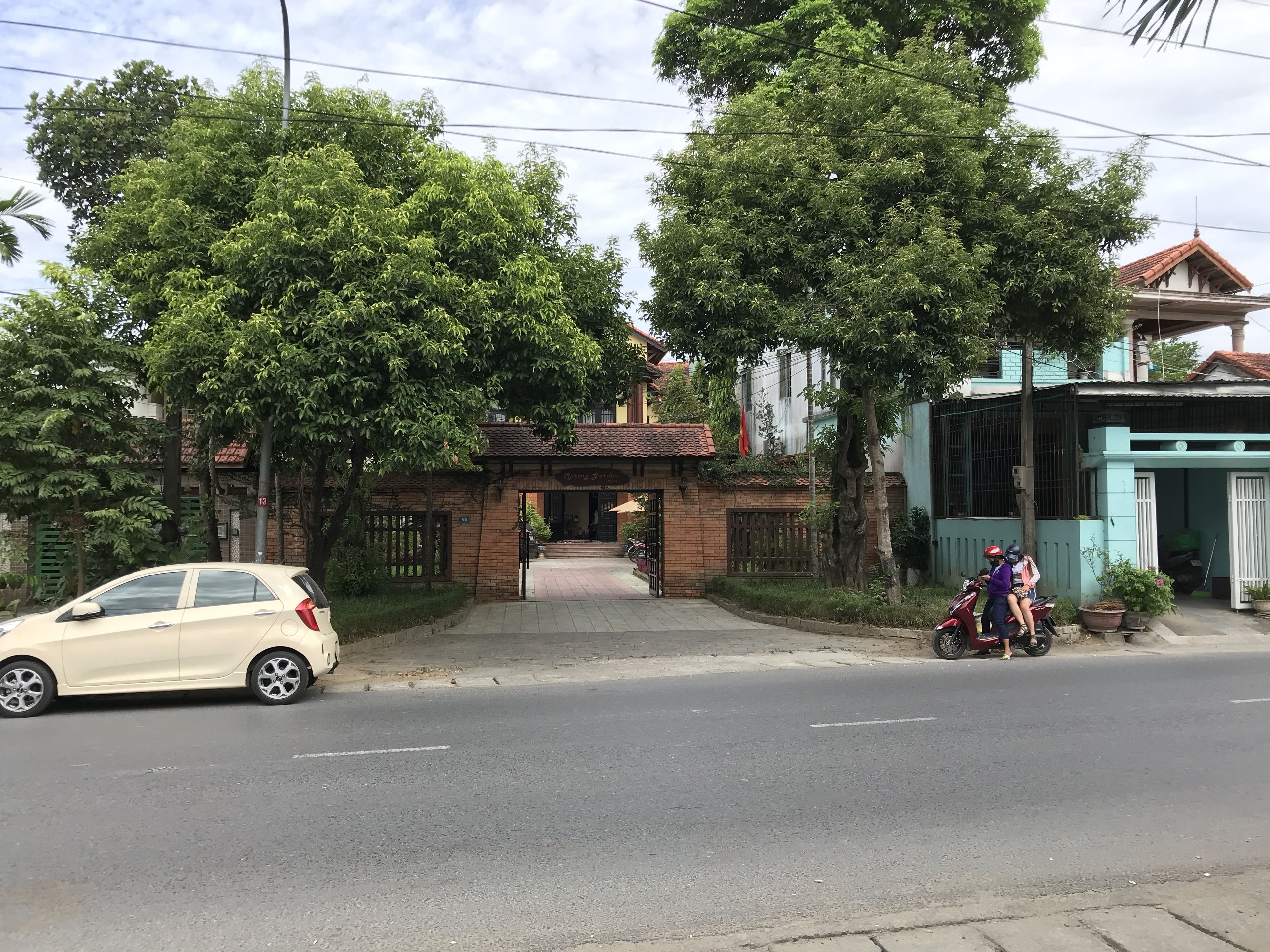 A building with a gated entrance, a parked car, and a motorcycle with two riders.