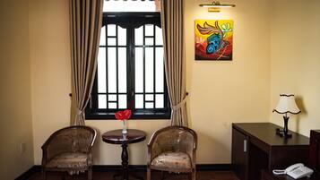 A room with two chairs, a small table with a vase, a painting, a lamp, and a phone on a desk.