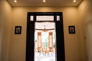 A doorway leading to a dining area with tables and chairs, framed pictures on the walls, and a ceiling light.