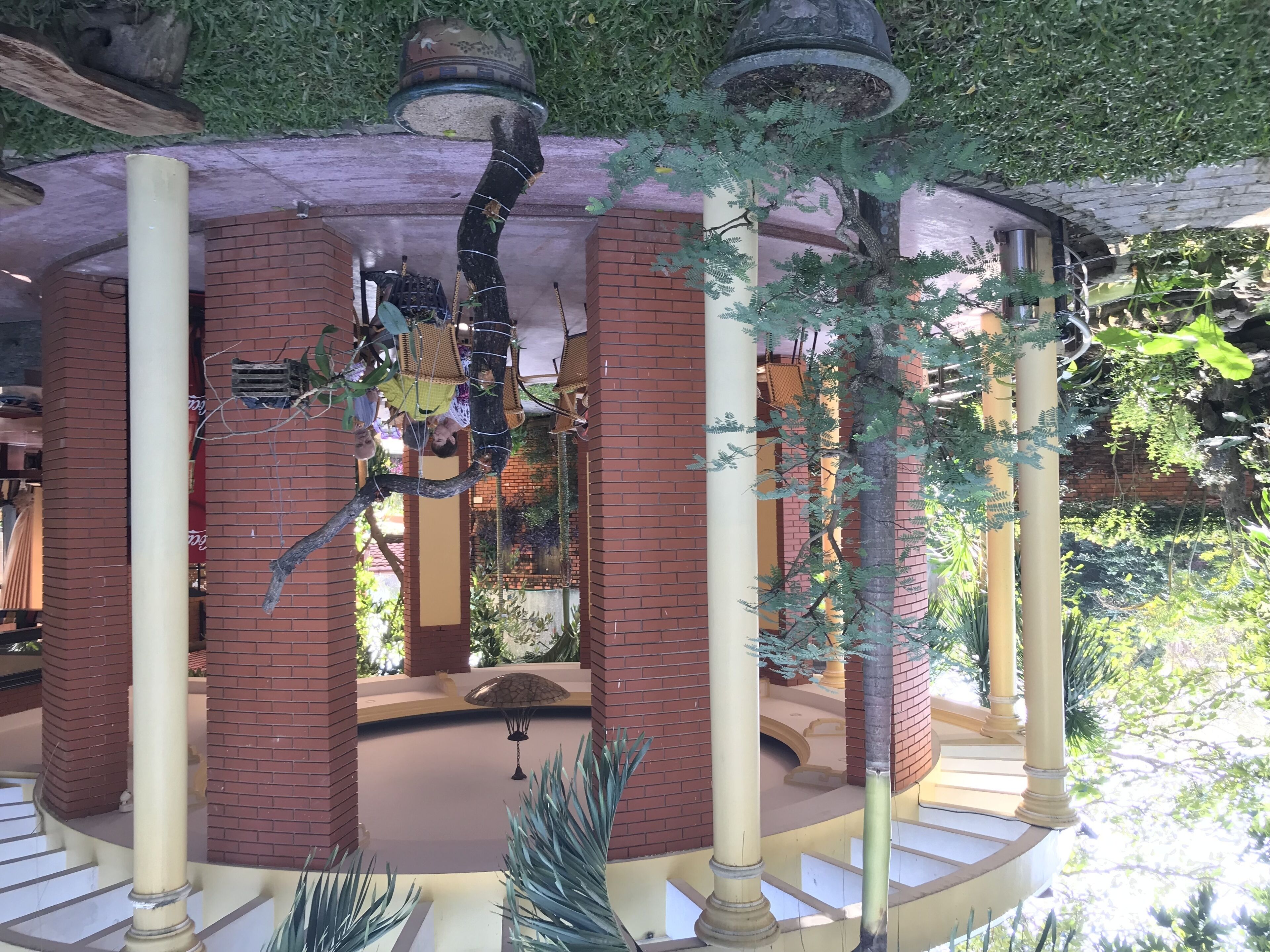 A covered outdoor area with brick pillars, a central fountain, and hanging plants.