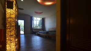A room with a wooden floor, a bed, a window with curtains, and a wall-mounted light fixture.