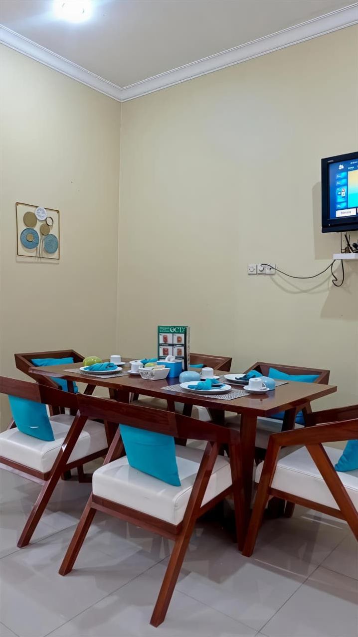 Un comedor con una mesa y sillas de madera, un televisor pequeño montado en la pared y un tablón de anuncios con adornos circulares.
