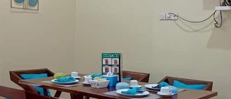 Un comedor con una mesa y sillas de madera, un televisor pequeño montado en la pared y un tablón de anuncios con adornos circulares.