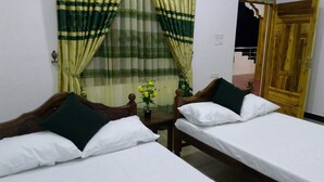 A room with two single beds, a wooden headboard, a small table with a vase of flowers, and a wooden door. - Nilaveli Star View Hotel (Nilaveli)