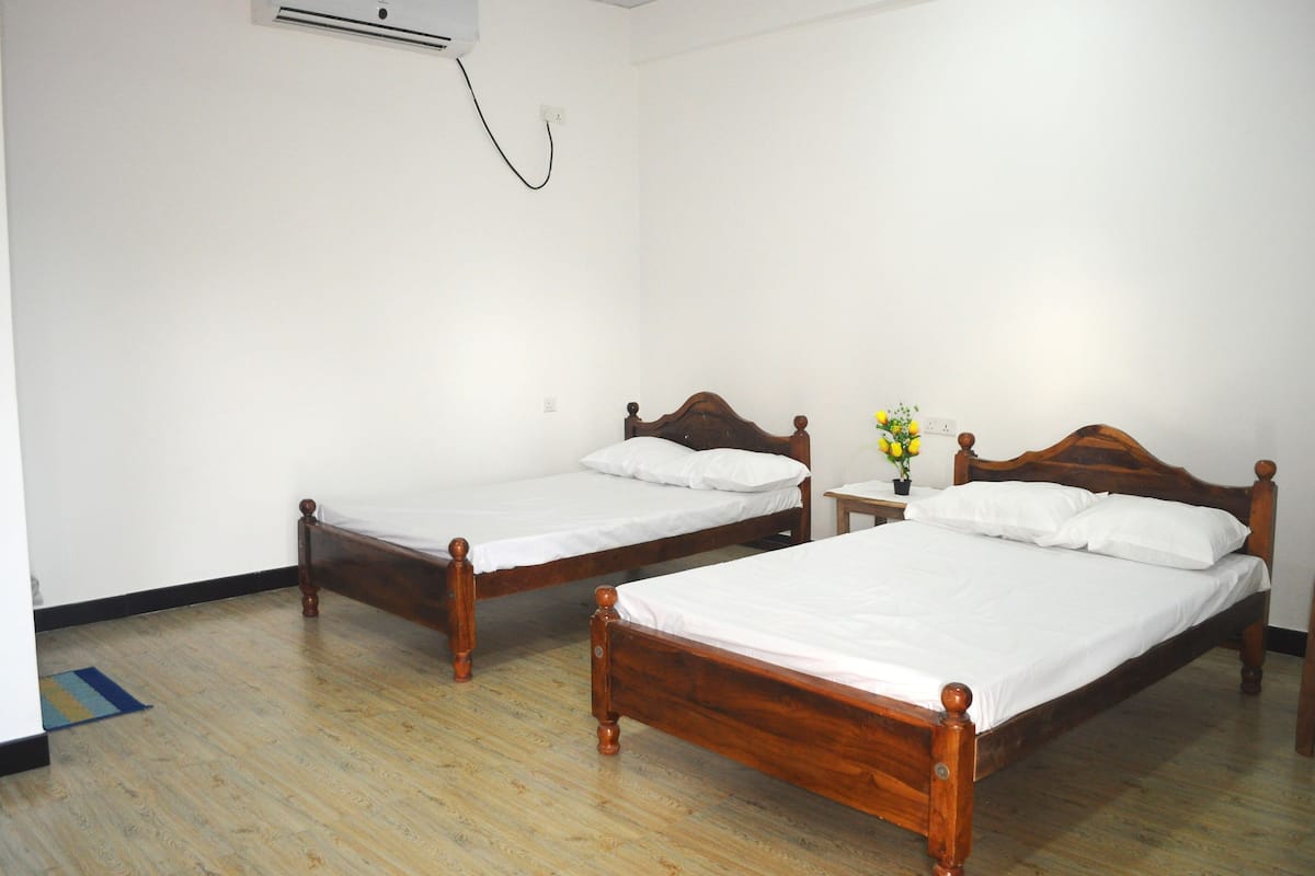 Una habitación con dos camas de madera, una mesita con un florero y un equipo de aire acondicionado en la pared.