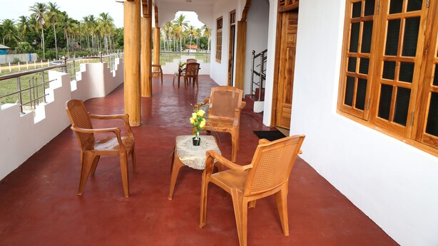 A covered balcony with wooden chairs and a small table, palm trees in the background, and a view of the surrounding area. - Nilaveli Star View Hotel (Nilaveli)