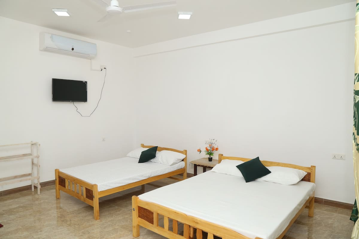 Una habitación con dos camas de madera, un televisor de pantalla plana en la pared y un ventilador de techo.