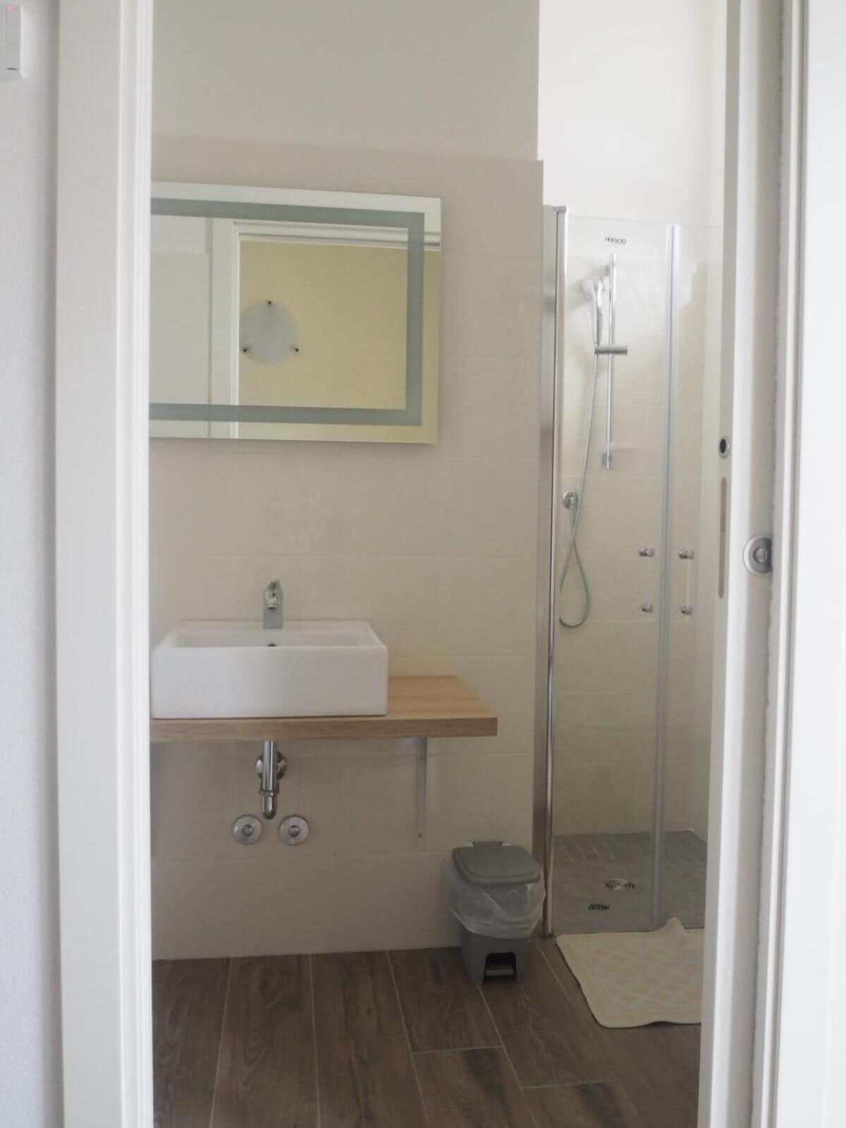 A small bathroom with a white sink, a mirror, and a glass shower enclosure.