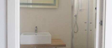 A small bathroom with a white sink, a mirror, and a glass shower enclosure.