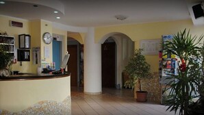 A reception area with a counter, a clock, a notice board, and potted plants. - Hotel Frida (Rimini)