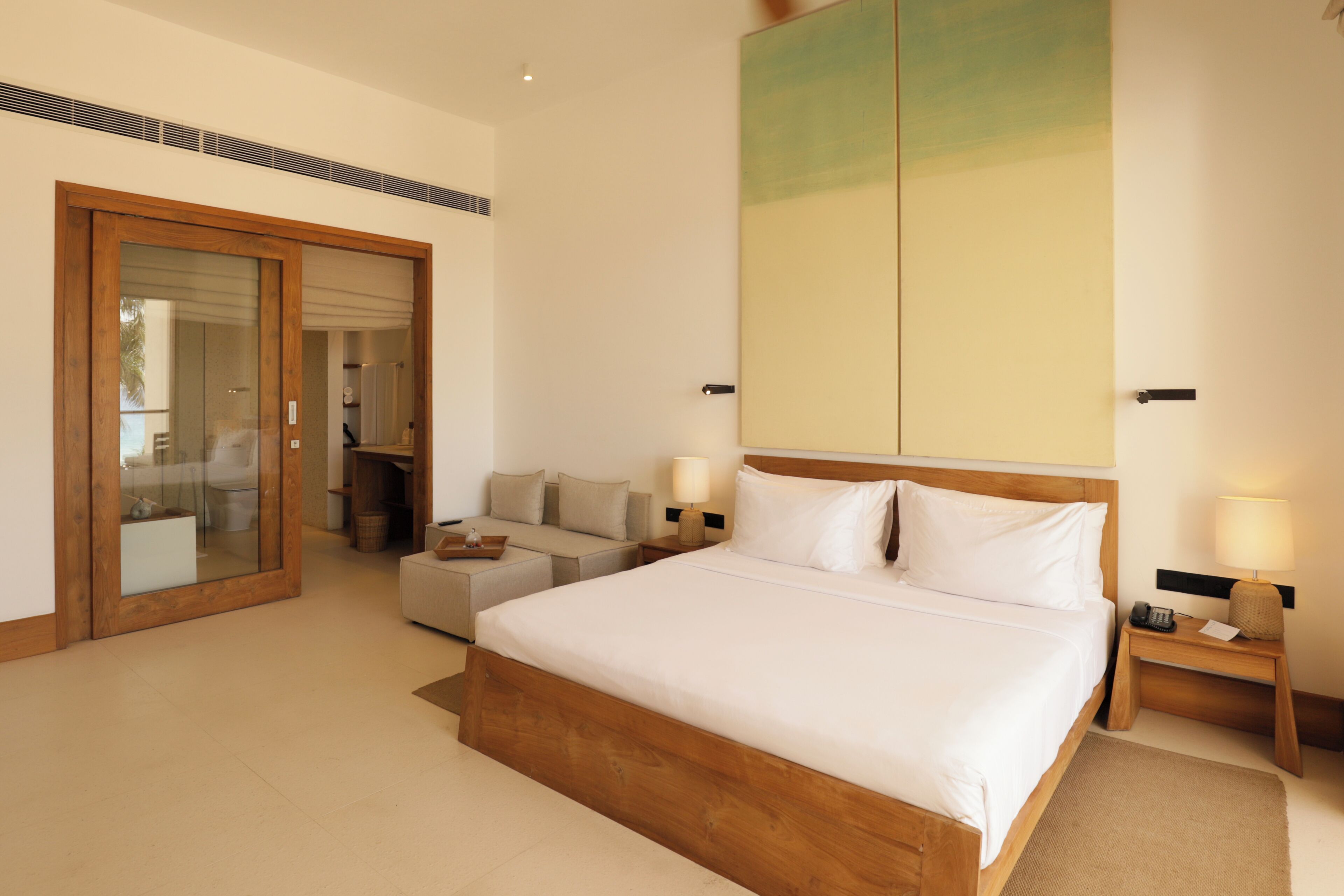 Habitación de hotel con una cama grande, un sofá, un escritorio y una puerta corredera que da a un balcón.