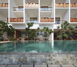A multi-story hotel with a central swimming pool, outdoor seating, and wooden balconies.