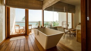 Een moderne badkamer met een vrijstaand bad, houten vloer en grote ramen met uitzicht op de oceaan.
