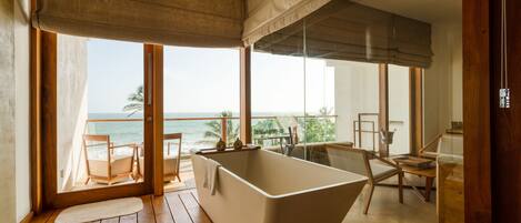 A modern bathroom with a freestanding bathtub, wooden flooring, and large windows offering a view of the ocean.