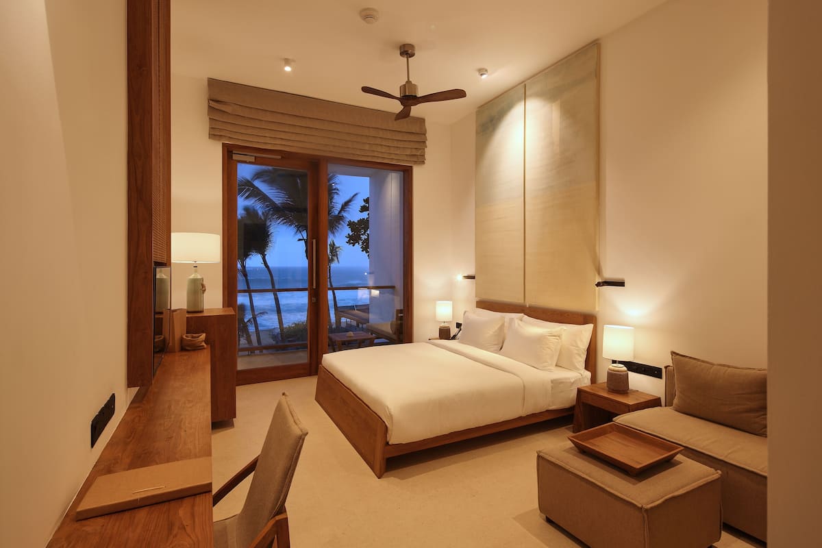 Quarto de hotel moderno com cama, escrivaninha, poltrona, sofá e varanda com vista para o mar.