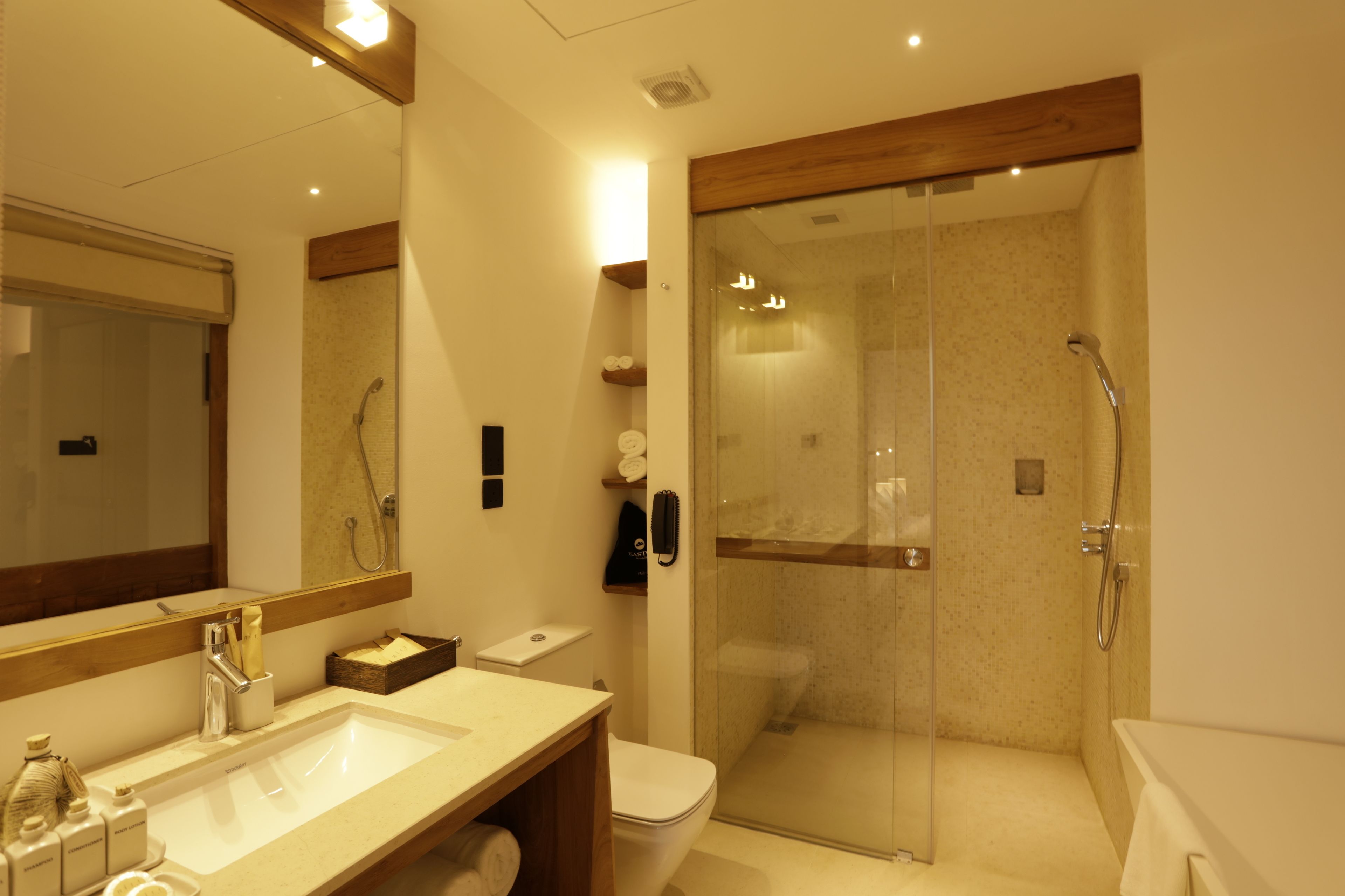 A modern bathroom with a large mirror, a sink, a toilet, and a glass-enclosed shower area.
