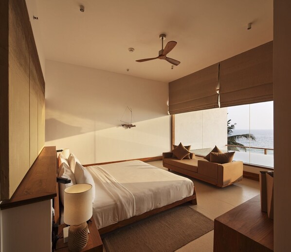 A modern bedroom with a large bed, a sofa, a ceiling fan, and a view of the ocean. - Riff Hikkaduwa (Hikkaduwa)