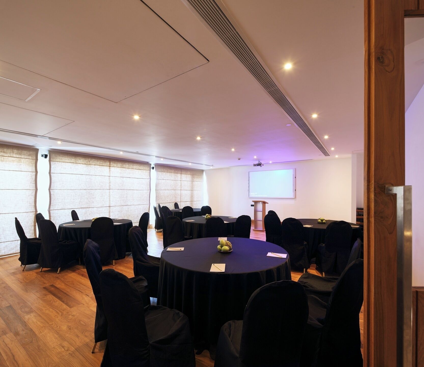A conference room with round tables, black chairs, a projector screen, and a large window.