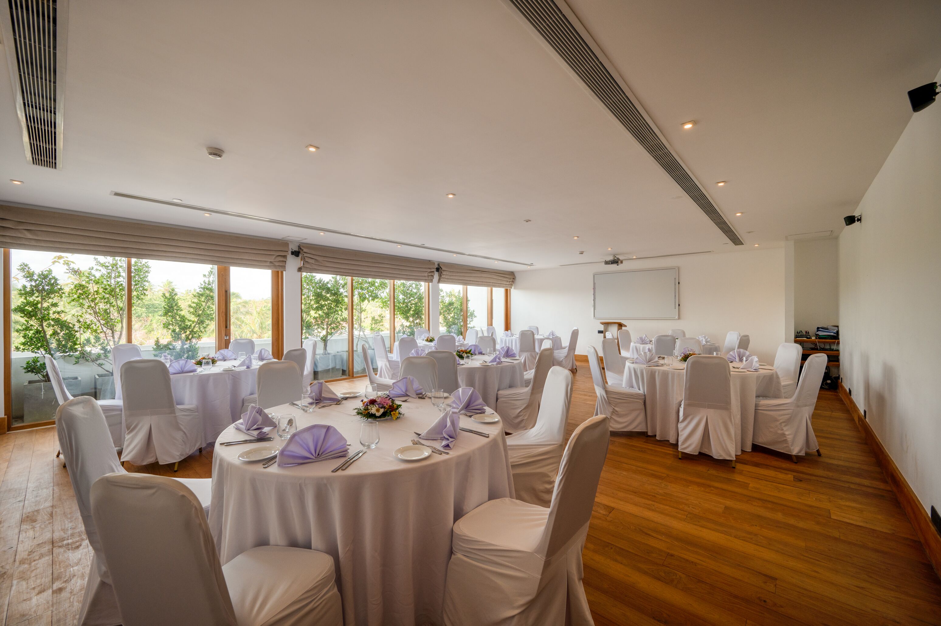 A banquet hall with round tables set for events, large windows, and a white ceiling.