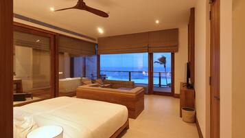 A bedroom with a large bed, a ceiling fan, a view of the ocean, and a balcony.