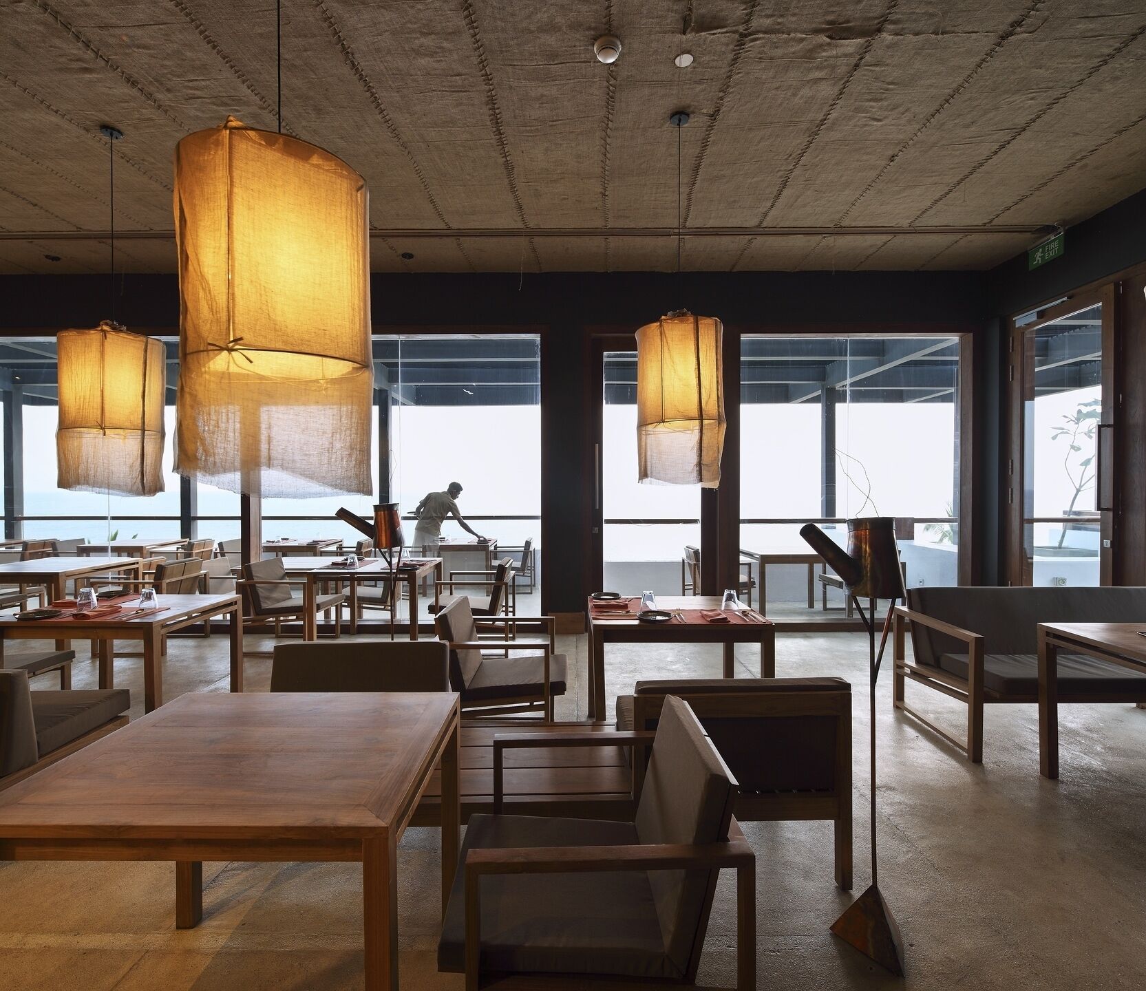 Un restaurant spacieux avec de hauts plafonds et de grandes fenêtres, doté de tables et de chaises en bois, ainsi que de lanternes en papier suspendues.