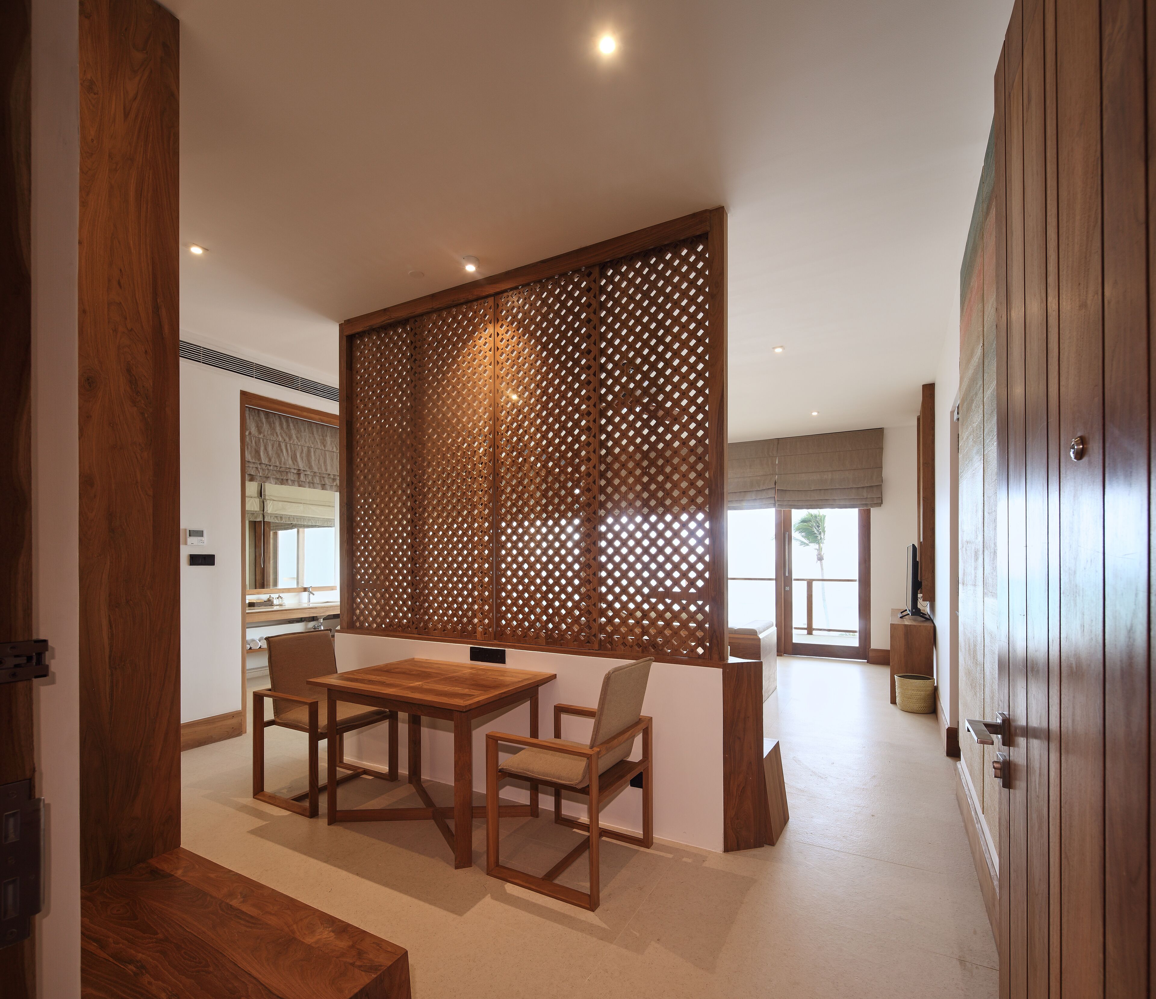 A room with a wooden table and chairs, a partition with a lattice design, and a view of the outdoors.