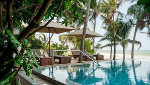 An infinity pool with lounge chairs and umbrellas, surrounded by palm trees and a beach view.