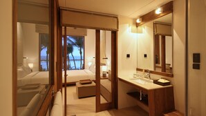 Een hotelkamer met een bed, een badkamer met wastafel en spiegel, en uitzicht op de oceaan door een raam.