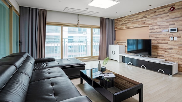 Un salon moderne avec un canapé en cuir, une table basse, un téléviseur à écran plat et un mur décoratif en bois.