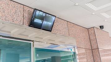Une caméra de surveillance est fixée au plafond, au-dessus d’un mur recouvert de carreaux et d’une porte vitrée.