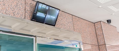 Cámara de seguridad montada en un techo con pared de azulejos y puerta de vidrio debajo.