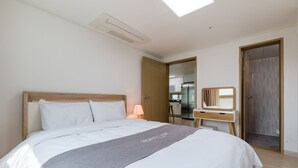 Une chambre d’hôtel avec un lit, un bureau, un miroir et une salle de bain visible à travers une porte ouverte.