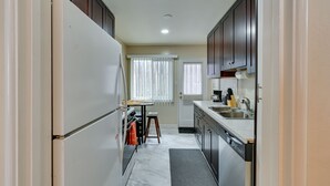 Cocina pequeña y funcional con refrigerador, estufa y lavamanos. Hay una ventana con persianas y una puerta con ventanal.
