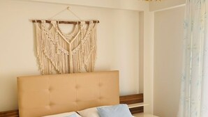 Una cama bien tendida con un adorno de macramé en la pared, un cabecero de madera y una lámpara colgante.