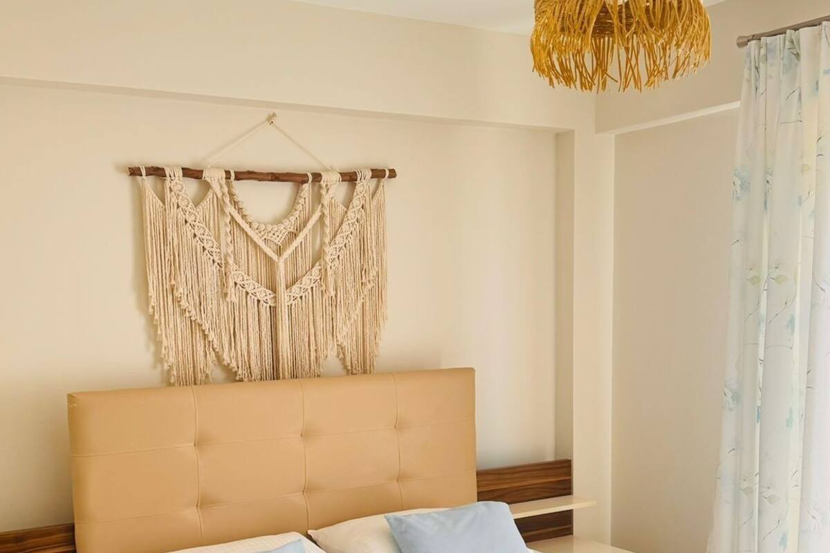 Cama bem arrumada com um pendente de macramé, cabeceira de madeira e luminária suspensa.
