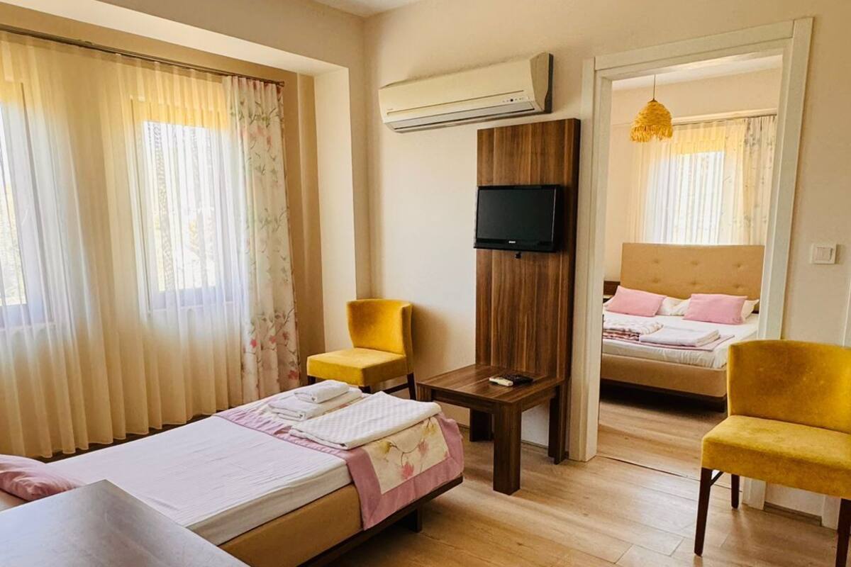 Quarto de hotel com piso de madeira, uma cama, uma escrivaninha, uma televisão e duas cadeiras.