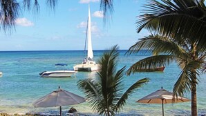Una spiaggia con una barca a vela, palme e ombrelloni.