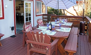 Una terraza exterior con mobiliario de madera, incluyendo sillas y una mesa lista para comer, con una parrilla y una sombrilla.