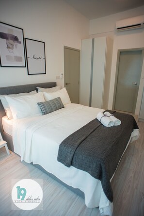 A neatly made bed with white linens and a gray throw blanket, a gray pillow, and two rolled towels on the bed. There is a framed picture with the word "love" on the wall above the bed.