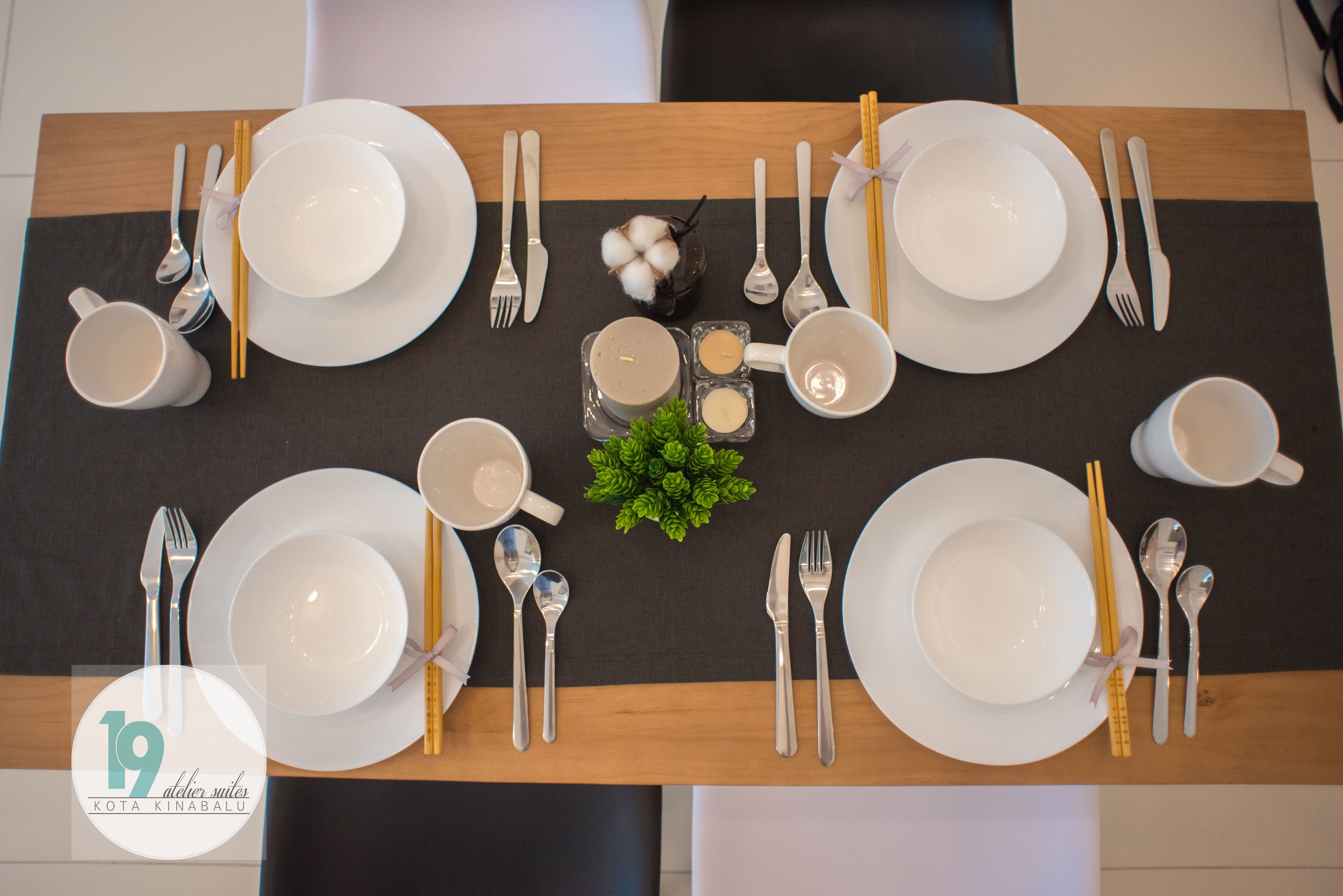 A neatly set dining table with plates, bowls, cutlery, and a small decorative plant.