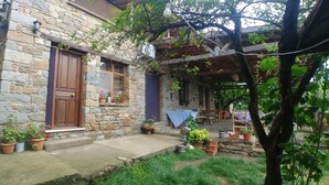 A stone building with a wooden door and windows, surrounded by potted plants and a tree. - Kastro Konak Boutique Otel (Gökçeada)