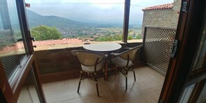 A balcony with a table and chairs, offering a view of a valley and mountains.