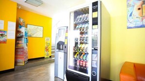 A vending machine in a hallway with yellow walls, a map on the wall, and a trash bin. - Residence Igea (Rimini)