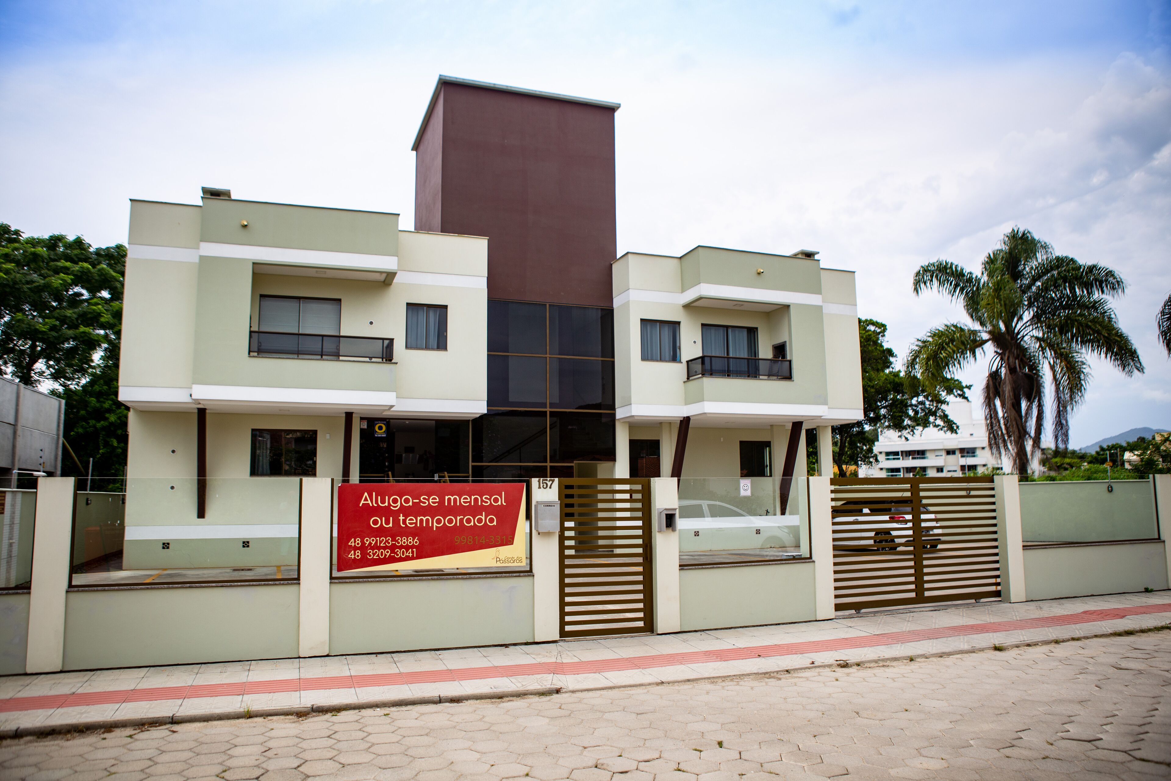 A modern two-story building with a prominent brown section, a gated entrance, and a signboard.