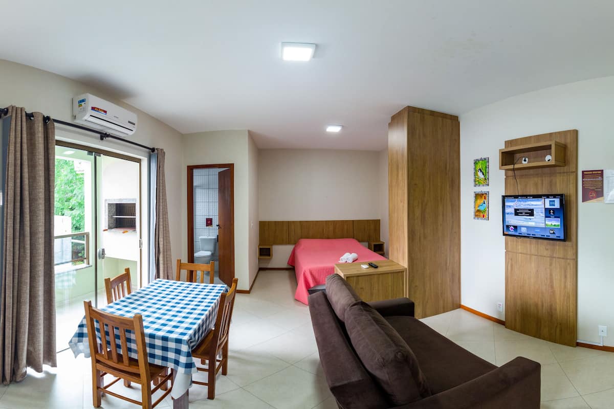 Een hotelkamer met een bed, een televisie, een tafel met stoelen, een bank en een airconditioner.