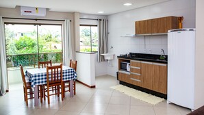 A modern kitchen with wooden cabinets, a white refrigerator, and a dining area with a checkered tablecloth. - Canto Dos Passaros Flat Canasvieiras (Florianópolis)