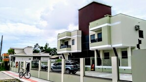A modern building with a flat roof, large windows, and a mix of green and white exterior walls. - Canto Dos Passaros Flat Canasvieiras (Florianópolis)